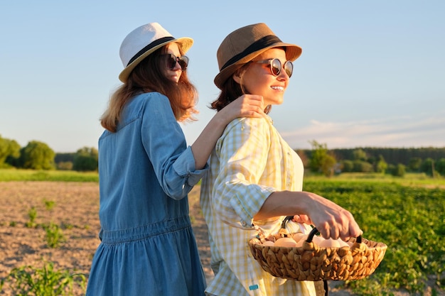 Agricultura, cultivo de produtos ecológicos orgânicos. Mãe e filha de mulheres com cesta de ovos, estilo de vida, natureza, jardim, pôr do sol, plano de fundo do campo