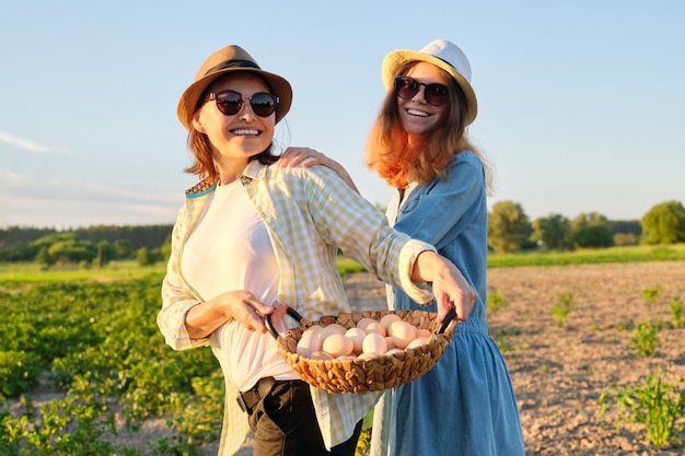 Agricultura, cultivo de productos ecológicos orgánicos. Mujeres madre e hija con canasta de huevos, estilo de vida, naturaleza, jardín, puesta de sol, fondo del campo