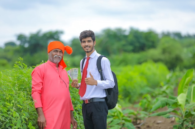 Agrónomo y agricultor indio mostrando rupia india en el campo