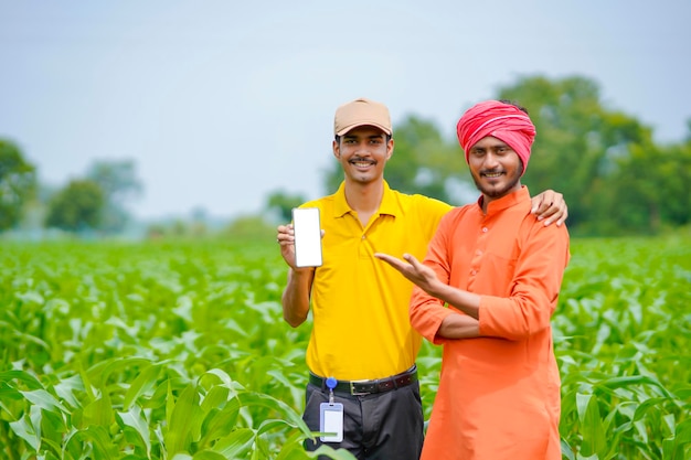 Agrônomo indiano mostrando smartphone com agricultor no campo de agricultura.