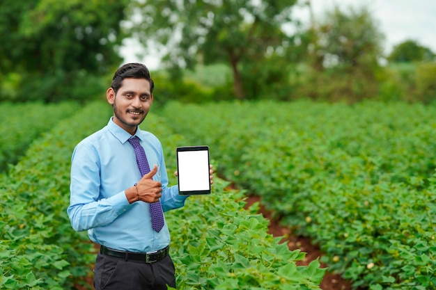 Agrónomo indio joven o un oficial que muestra la tableta en el campo de la agricultura.