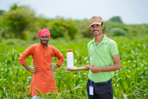 Agrónomo indio joven que sostiene la botella de fertilizante líquido con el agricultor en el campo de la agricultura verde.