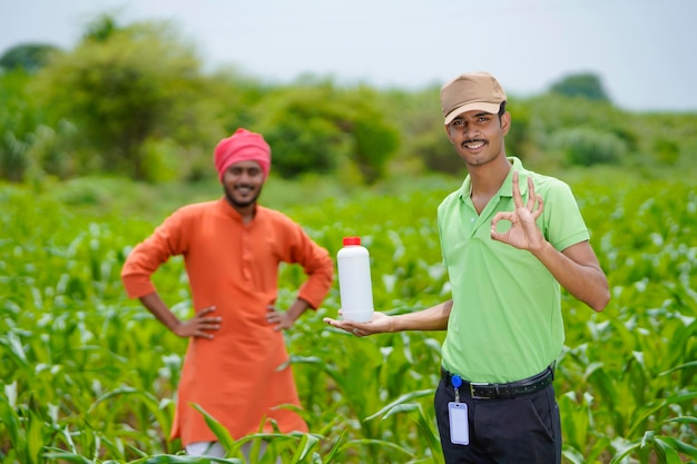 Agrónomo indio joven que sostiene la botella de fertilizante líquido con el agricultor en el campo de la agricultura verde.