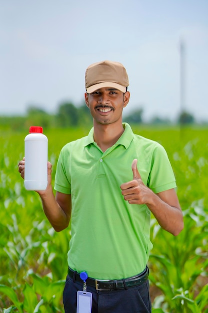 Agrónomo indio joven que sostiene la botella de fertilizante líquido en el campo de la agricultura verde.