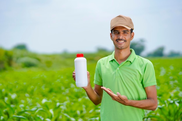 Agrónomo indio joven que sostiene la botella de fertilizante líquido en el campo de la agricultura verde.