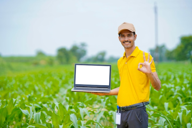 Agrónomo indio mostrando la pantalla del portátil en el campo de maíz.