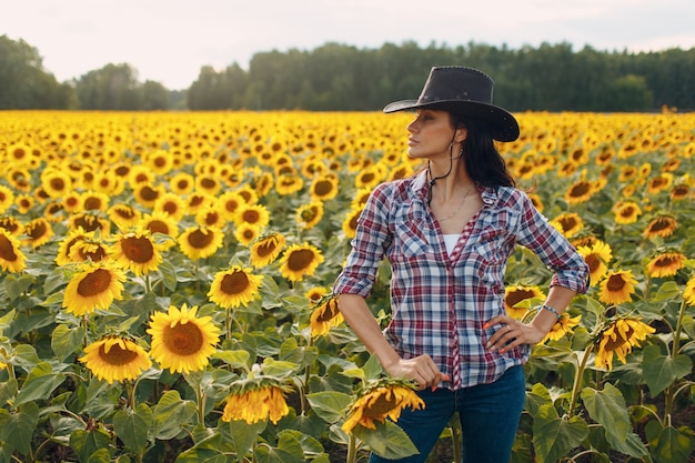 Agrónomo joven con sombrero de vaquero, camisa a cuadros y jeans en campo de girasol. Concepto de cosecha rica.