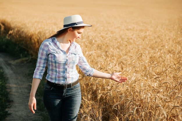 Agrónomo mujer con sombrero estudiando cosecha de trigo en el campo mujer de negocios analizando cosecha de grano ...