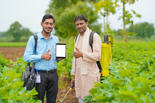 Agrónomo o banquero indio joven que muestra la tableta con el agricultor en el campo de la agricultura.