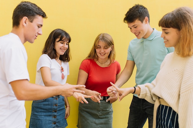 Agrupe a los adolescentes que juegan el juego de papel de las tijeras de la roca sobre fondo amarillo.