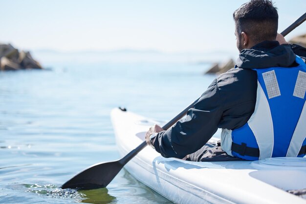 El agua abierta es una carretera a la aventura Vista trasera de un joven en kayak en un lago