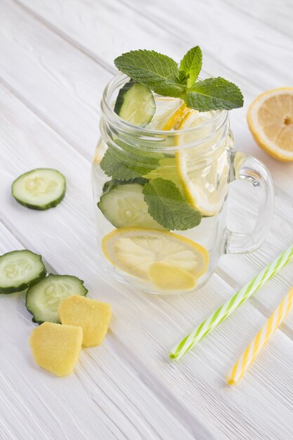 Agua atrevida para adelgazar o infundir agua con limón, pepino y jengibre en el vaso sobre el fondo de madera blanca. Ubicación vertical.