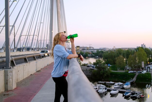 Foto Água bebendo da mulher sedento no exercício ao ar livre na ponte da cidade.