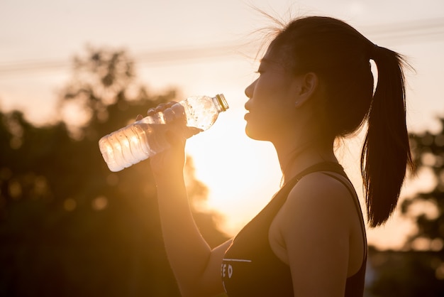 Agua de bebida de mujer en el fondo del atardecer