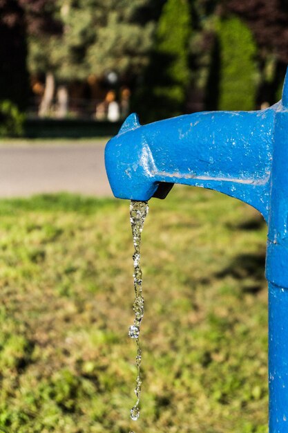 Água caindo da torneira azul em um dia ensolarado