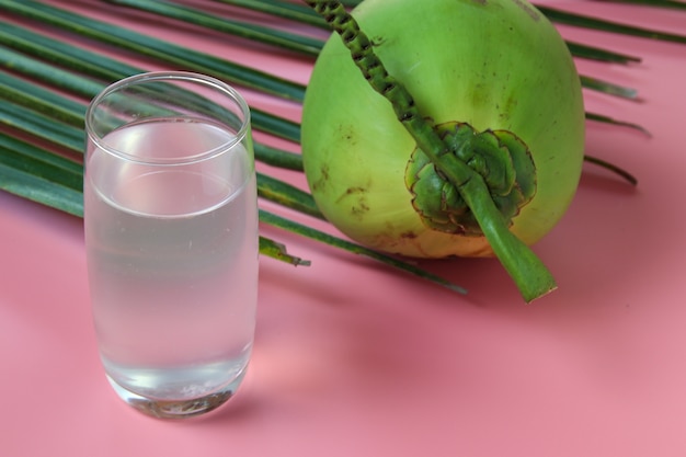 Agua de coco fresca en vidrio Listo para beber con la hoja en fondo rosa, concepto de verano