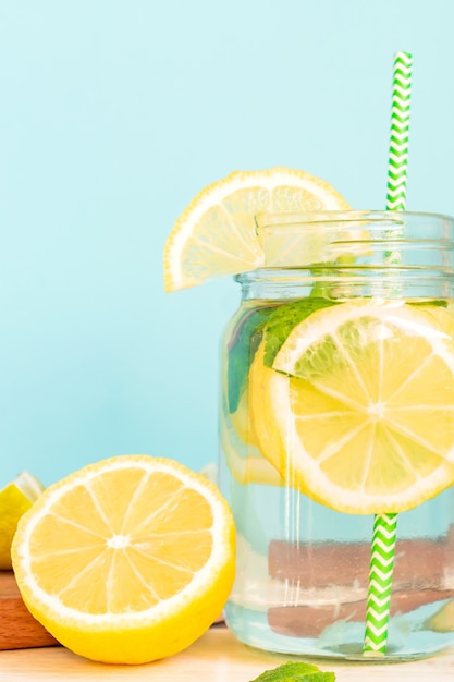 Água de limonada cítrica com fatias de limão e hortelã, água saudável e desintoxicação bebe no verão na mesa de madeira com azul iluminar o fundo