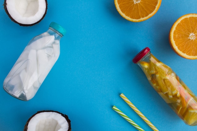 Agua de desintoxicación con coco y naranja en las botellas de vidrio sobre el fondo azul.Vista superior. Copiar el espacio.