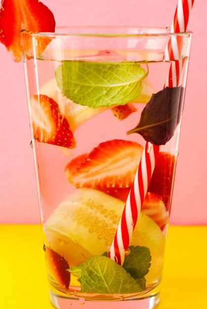 Foto agua de desintoxicación con fresa y pepino en vidrio sobre el fondo rosa y amarillo.