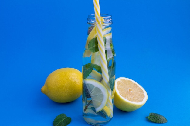 Agua de desintoxicación con limón y menta en la botella de vidrio sobre fondo azul.