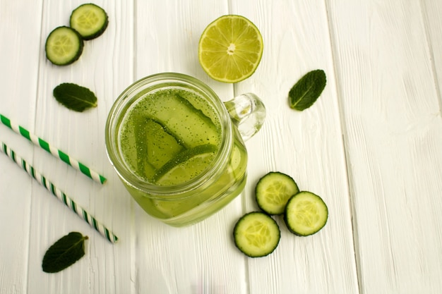 Agua de desintoxicación con pepino y lima en la superficie de madera blanca. Vista superior.