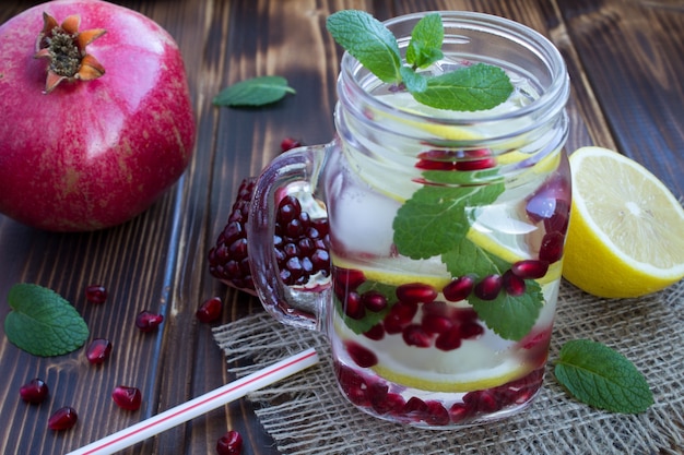 Agua detox con granada, limón y menta en el fondo rústico