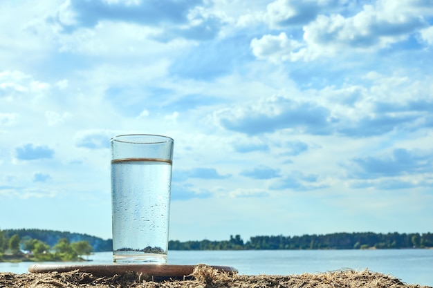 Agua dulce clara en un vaso contra el fondo del río. Agua natural ecológica.