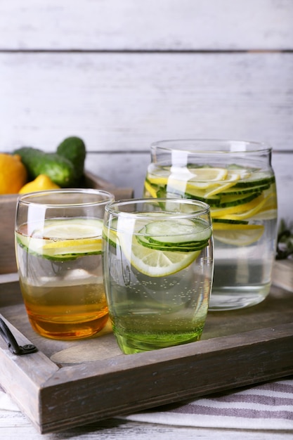 Agua dulce con limón y pepino en cristalería en bandeja de madera closeup