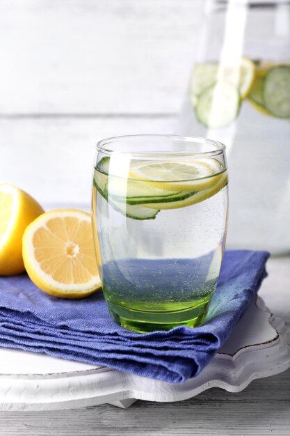 Agua dulce con limón y pepino en cristalería sobre fondo de madera