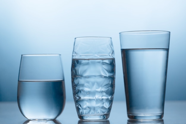 Foto agua dulce en tres vasos sobre el fondo azul con reflejo