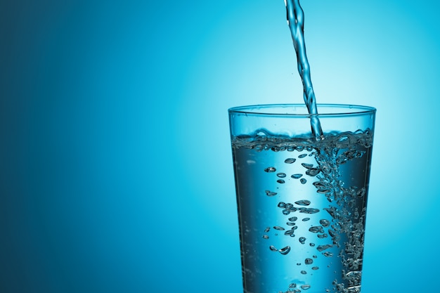 Foto el agua dulce se vierte en un vaso sobre un fondo azul.