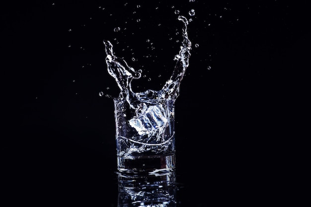 Agua fría aislada en un vaso con salpicaduras y cubitos de hielo sobre negro, brandy en un vaso