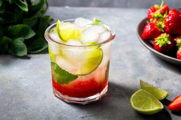 Agua fría de desintoxicación con menta fresa lima en el vaso con cubitos de hielo sobre fondo gris