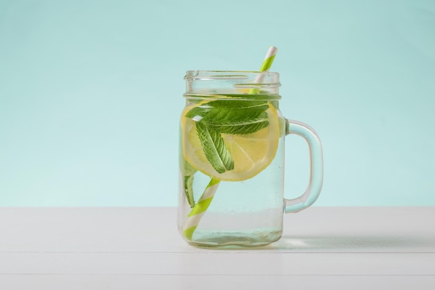 Agua fría con limón y menta en una copa de vidrio sobre una mesa blanca