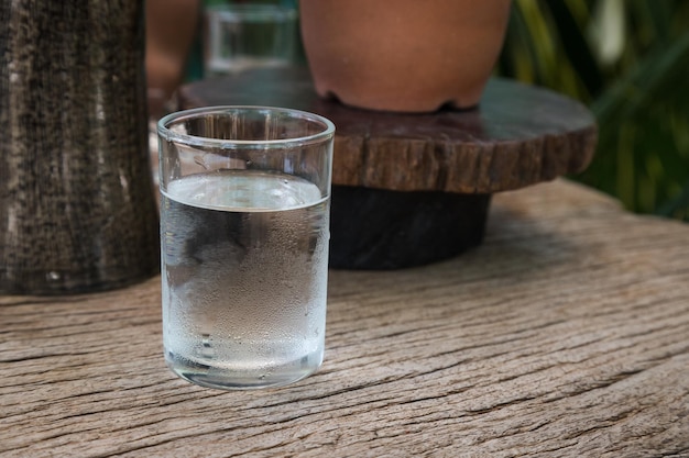 Agua fría en taza puesta en una mesa de madera de corteza con alguna decoración natural en el fondo