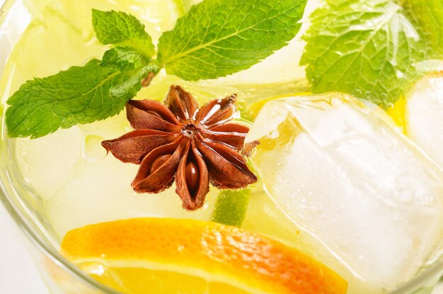 Agua de frutas de lima y naranja con hielo y menta sobre mesa blanca