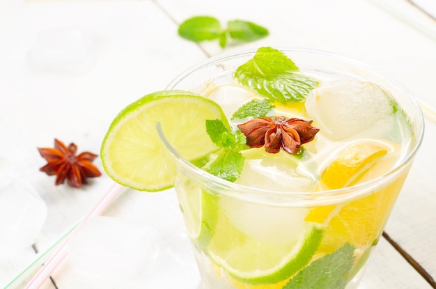 Agua de frutas de lima y naranja con hielo y menta sobre mesa blanca