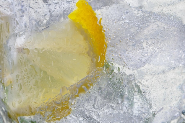 Agua con gas con limones y cubitos de hielo en vaso de cerca