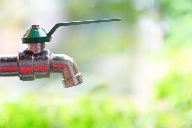 Agua del grifo que gotea con el fondo verde de la naturaleza - concepto de ahorro de agua