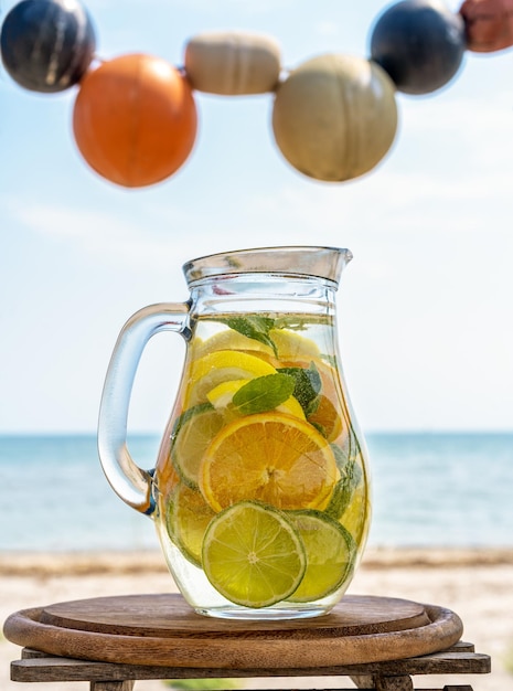 Agua infundida de desintoxicación con limón, naranjas y menta con vista a la costa del mar