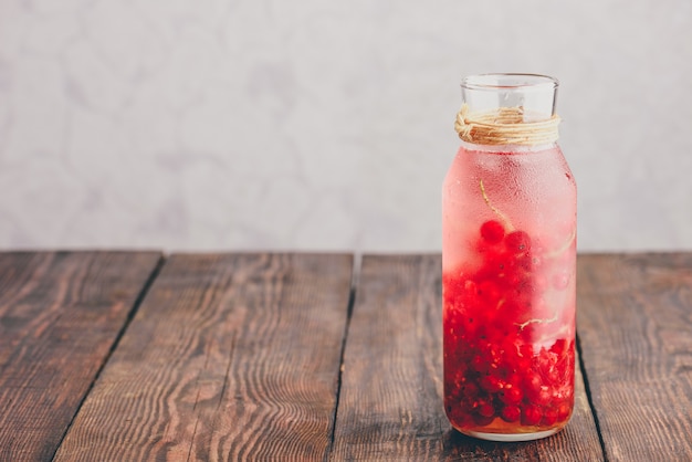 Agua de infusión de grosella roja con hielo en botella de vidrio