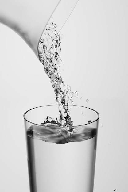 El agua de una jarra se vierte en un vaso de vidrio lleno de agua sobre un fondo blanco d render