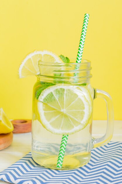 Agua de limonada cítrica con limón y menta en rodajas, bebida de agua saludable y desintoxicante en verano en una mesa de madera con fondo amarillo