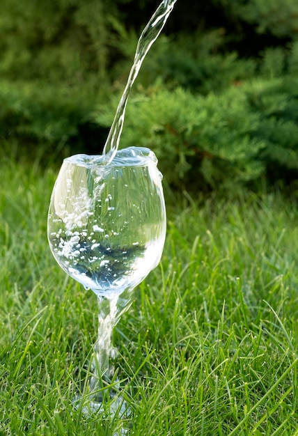 El agua limpia se vierte en una copa de vino transparente y se desborda de ella sobre la hierba verde