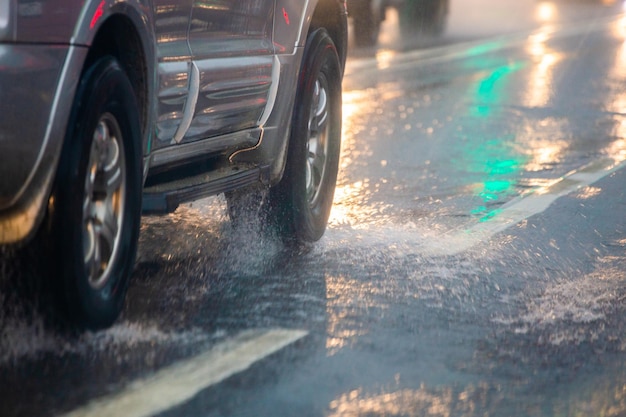 El agua de lluvia salpica el flujo de las ruedas de un camión plateado que se mueve rápido en la ciudad a la luz del día con un enfoque selectivo