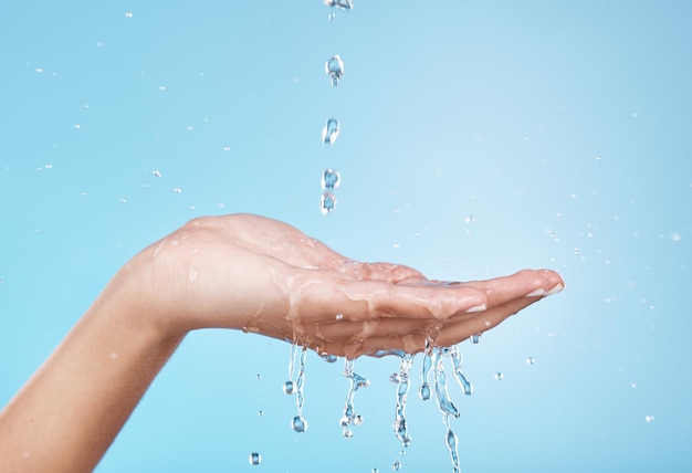 Foto agua de manos e hidratación con una mujer limpiando en un estudio sobre un fondo azul para higiene o cuidado personal salpicaduras de agua y cuidado de la piel con una mujer lavándose las manos en la ducha o el baño