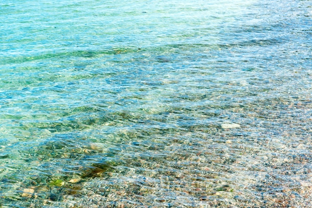 Agua de mar azul clara en la playa con guijarros