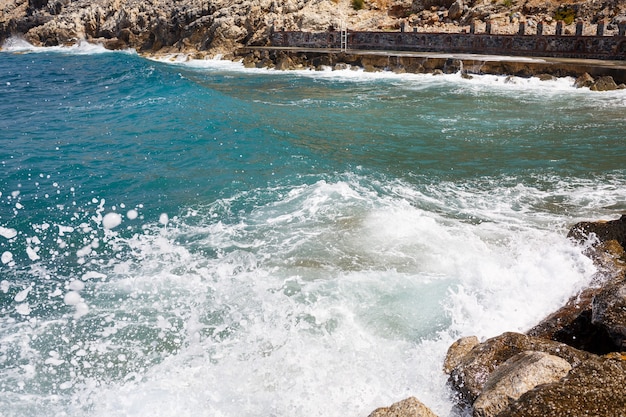 El agua de mar golpea contra las rocas rocosas y hace olas con espuma, muelle escarpado en el mar