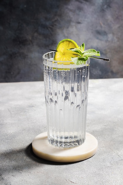 Água mineral gaseificada com limão e hortelã no copo em fundo cinza