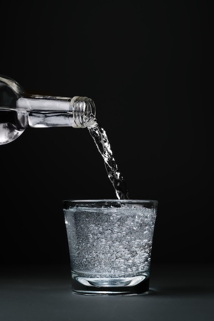 El agua mineral se vierte en un vaso, primer plano, pared oscura con espacio de copia, enfoque selectivo.